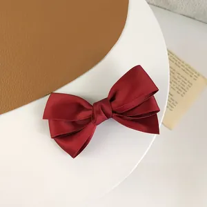 Close-up of a red triple-layer satin bow hair clip on a premium textured leather background