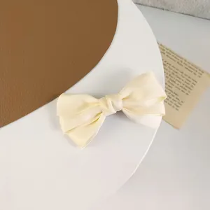 Close-up of triple-layered cream satin bow hair clip on a minimalist display
