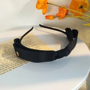 Détail d'un serre-tête en ruban gros-grain noir avec un nœud double et charme doré