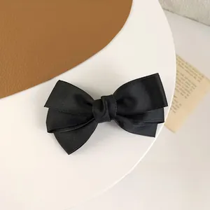 Close-up of black triple layered ribbon bow hair clip on elegant white tray and leather