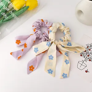 Floral print scrunchies with bow ribbons in purple and off-white fabric on white surface