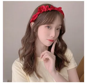 Detailed view of a bright red satin pleated headband with bow worn by a model