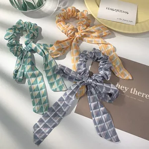 Three colorful geometric pattern scrunchies with long ribbons on a yellow background