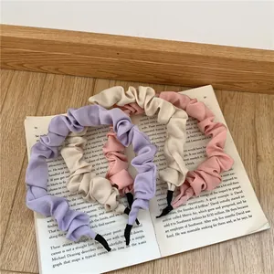 Close-up of pleated fabric headbands in purple, beige and pink set on an open book