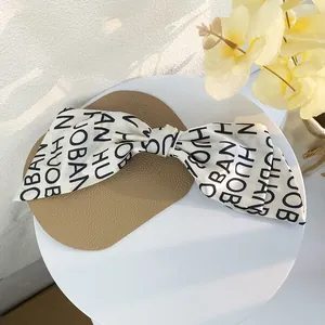 Close-up of cream fabric bow hair clip with black alphabet pattern and spring clip