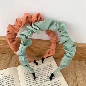 Detail of pleated fabric headbands in orange and mint green on a rustic wooden table