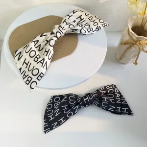 Detail of satin bow hair clips featuring a stylish monochromatic letter print pattern