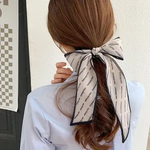Detail view of a cream chiffon bow hair tie with blue edges and FINE letter printing