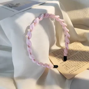 Dettaglio della fascia intrecciata rosa con catena dorata su elegante fondo in tessuto