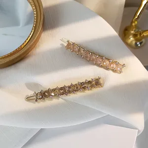 Detail view of two gold metal hair clips with champagne pink and amber beads on white fabric
