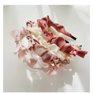 Close-up of pleated satin bow headbands in four soft pastel colors on glass
