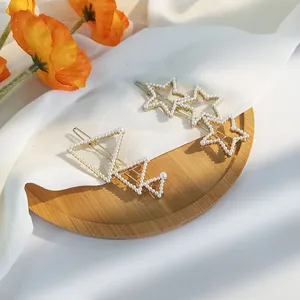 Star and triangle pearl hair clips set in gold finish on a decorative wooden tray