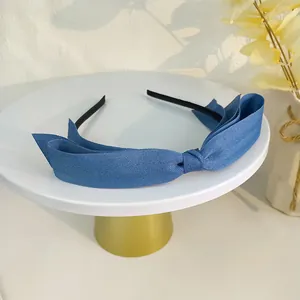 Vue détaillée d'un serre-tête bleu marine avec nœud en tissu sur un support blanc