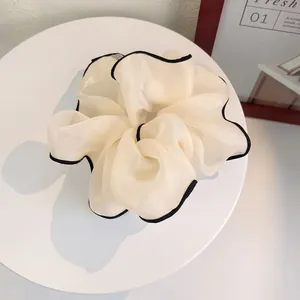 Detail of elegant beige organza scrunchie with black trim on a white display stand