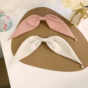 Détail de nœuds de cheveux en satin rose et crème avec pendentifs perles
