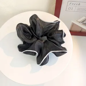 Detail of a large black mesh hair tie with silver trimmed edges on a white display stand