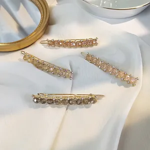 Close-up of four elegant gold-tone hair clips with colorful crystals on white silk