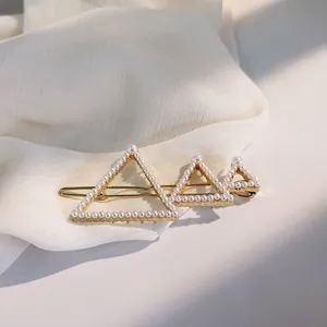 Detailed view of geometric gold pearl hair clip on elegant white chiffon fabric background