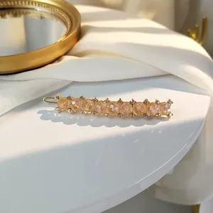 Detail of a golden hair clip featuring amber beads and micro-pave crystals on a silk surface