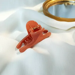 Detail of glossy coral orange hair claw clip with golden spring on white fabric