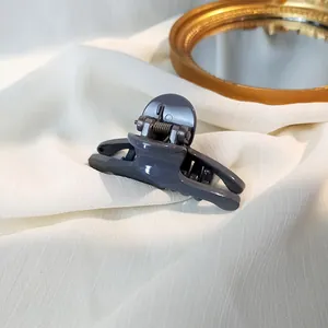 Macro detail of dark grey glossy hair claw clip with metallic spring on white fabric