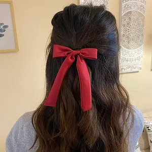 Detail view of a long red satin bow hair tie worn on wavy brunette hair in home setting