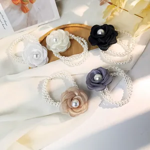 Detailed macro of five silk camellia flower hair ties with double-row pearl elastic bands