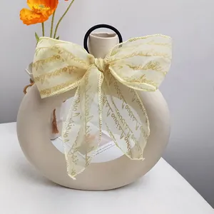 Elegant organza bow hair tie with gold Love text print displayed on white vase