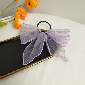 Detail of a purple mesh lace bow hair tie with silver scripts in a golden tray