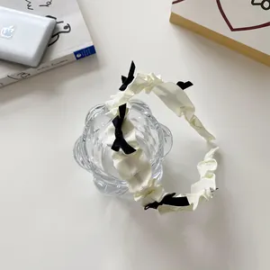 Détail d'un serre-tête plissé crème avec petits nœuds noirs décoratifs