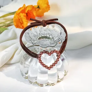 Detailed view of a brown elastic hair tie with a heart-shaped pearl pendant and bow