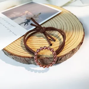 Detail of vintage elastic hair tie with pearlescent pink-brown beads on a rustic wood base