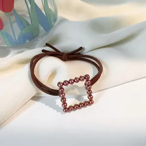 Vintage brown elastic hair tie with burgundy pearl square on soft beige background