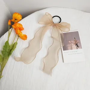 Detail of beige organza bow hair tie with long ribbons on white textured fabric