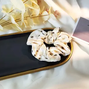 Close-up of beige plaid scrunchie with coffee geometric patterns on a gold-rimmed tray