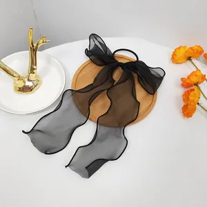 Detail of a black organza bow hair tie with long ribbons on a wooden tray decor