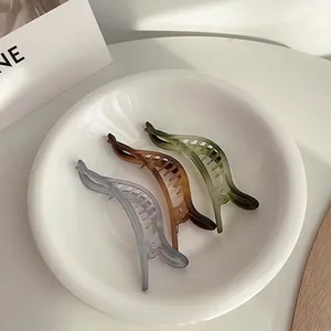 Tre fermagli a banana opachi in grigio, marrone e verde in un piatto di ceramica