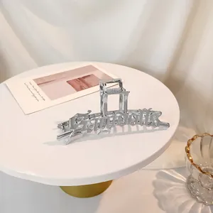 Pinza para el cabello de metal plateado con letras góticas en un pedestal minimalista