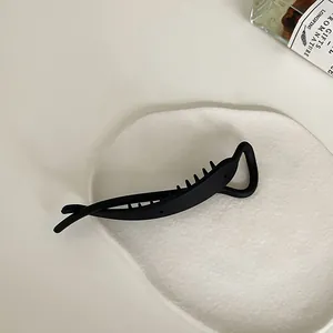 Detailed macro view of matte black banana hair clip on a minimalist white ceramic tray