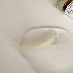 Close-up of matte cream translucent resin banana hair clip on a soft white fabric background