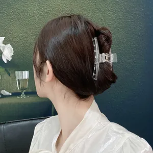 Close-up of a clear acrylic hair claw clip securing a hairstyle against a green wall