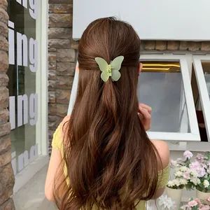 Pinza de mariposa verde claro mate en el cabello castaño ondulado de la modelo