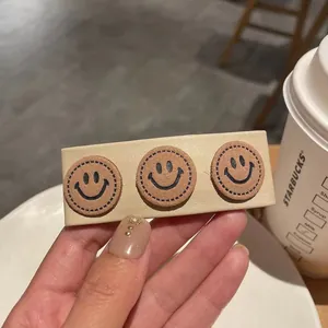Detail view of cream PU leather hair clip featuring cute brown stitched smiley faces