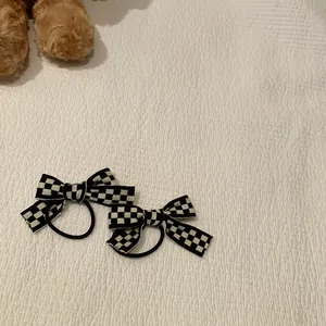 Gros plan de deux chouchous à nœuds en damier noir et blanc sur un tissu blanc texturé