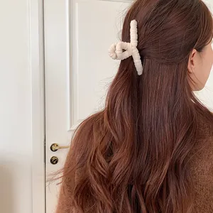 Close-up of a plush beige hair claw clip styled on long wavy hair in a cozy setting