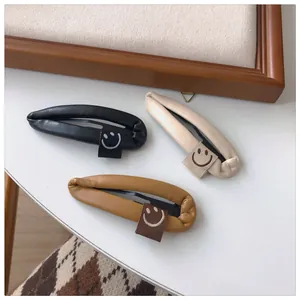 Detail of three PU leather teardrop hair clips in black, beige, and caramel with smiley face