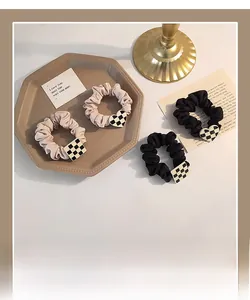 Detail of beige and black checkered scrunchies with heart and square charms on a tray