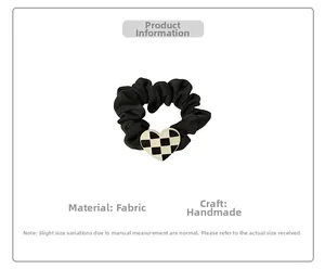 Detailed macro view of the handmade black pleated fabric hair tie with checkered heart charm