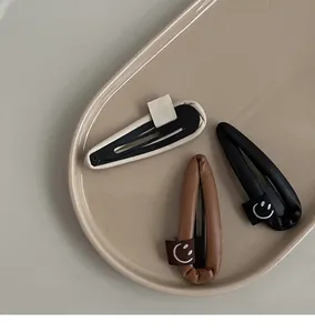 Close-up of PU leather waterdrop BB hair clips in cream, coffee and black with smile labels