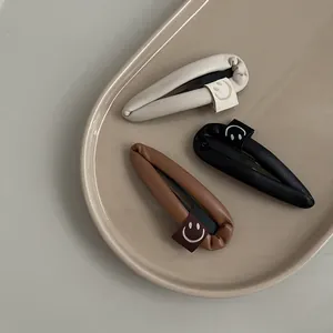 Close-up of PU leather waterdrop hair clips in cream and brown with smile pattern